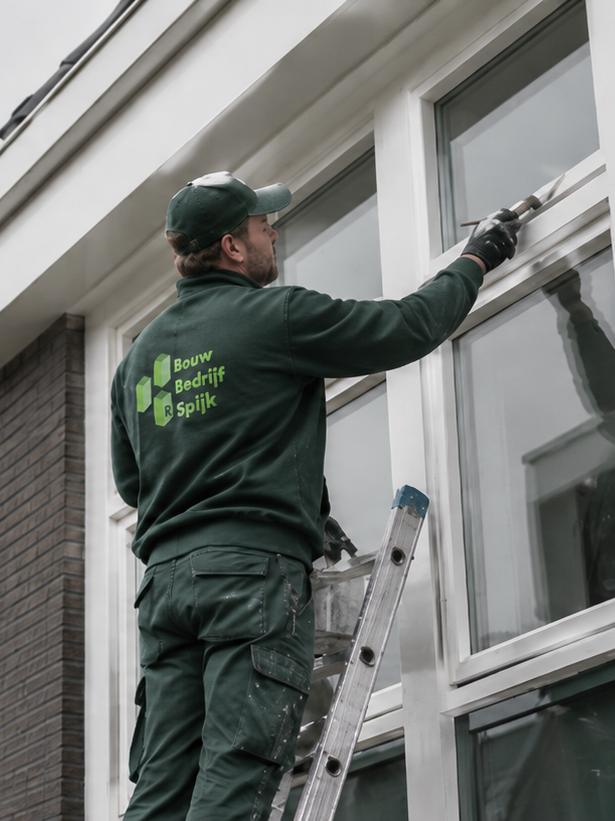 Schilder van Spijk schildert een houten kozijn op de ladder